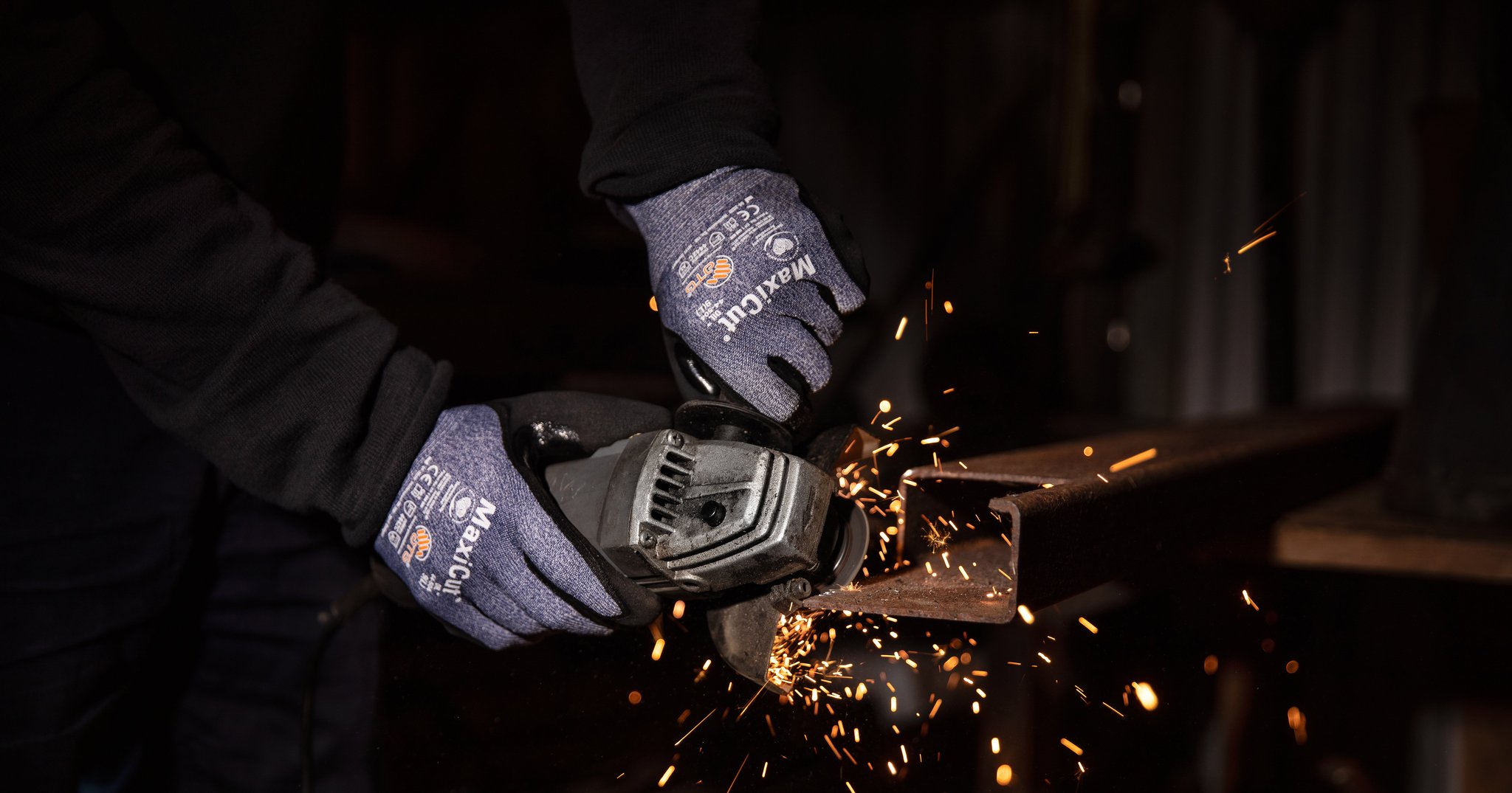 Person mit ATG MaxiCut Handschuhen schleift Metall mit einem Winkelschleifer – Funken fliegen in einer Werkstattumgebung.