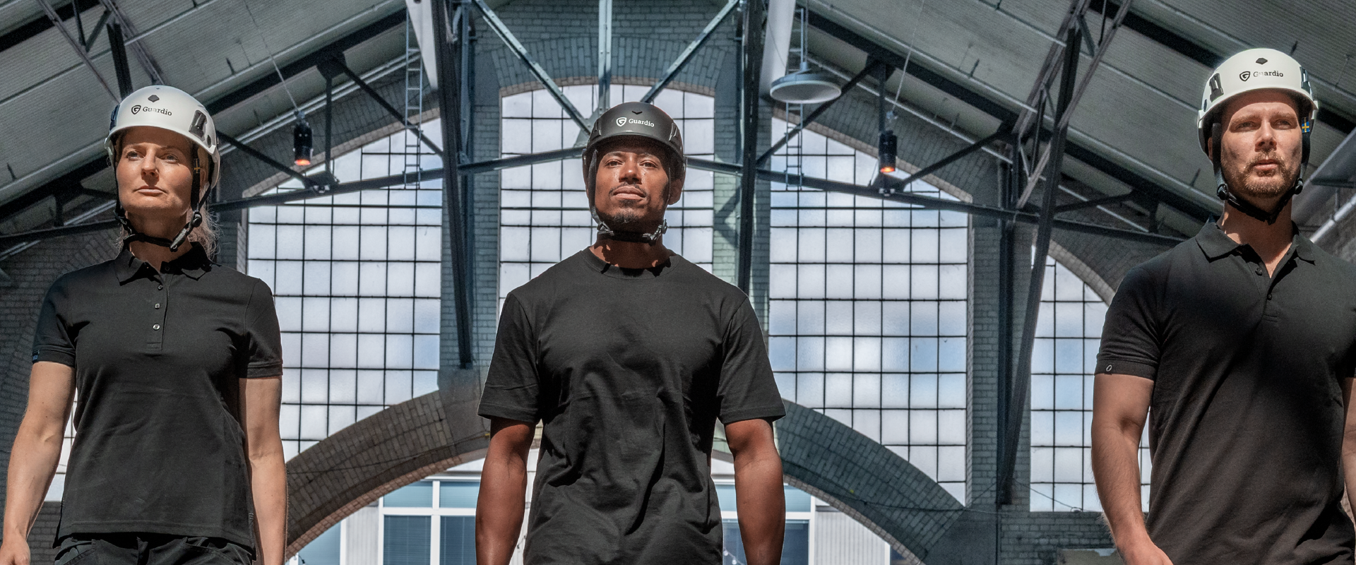 Three people wearing safety helmets walk towards the camera in an industrial environment