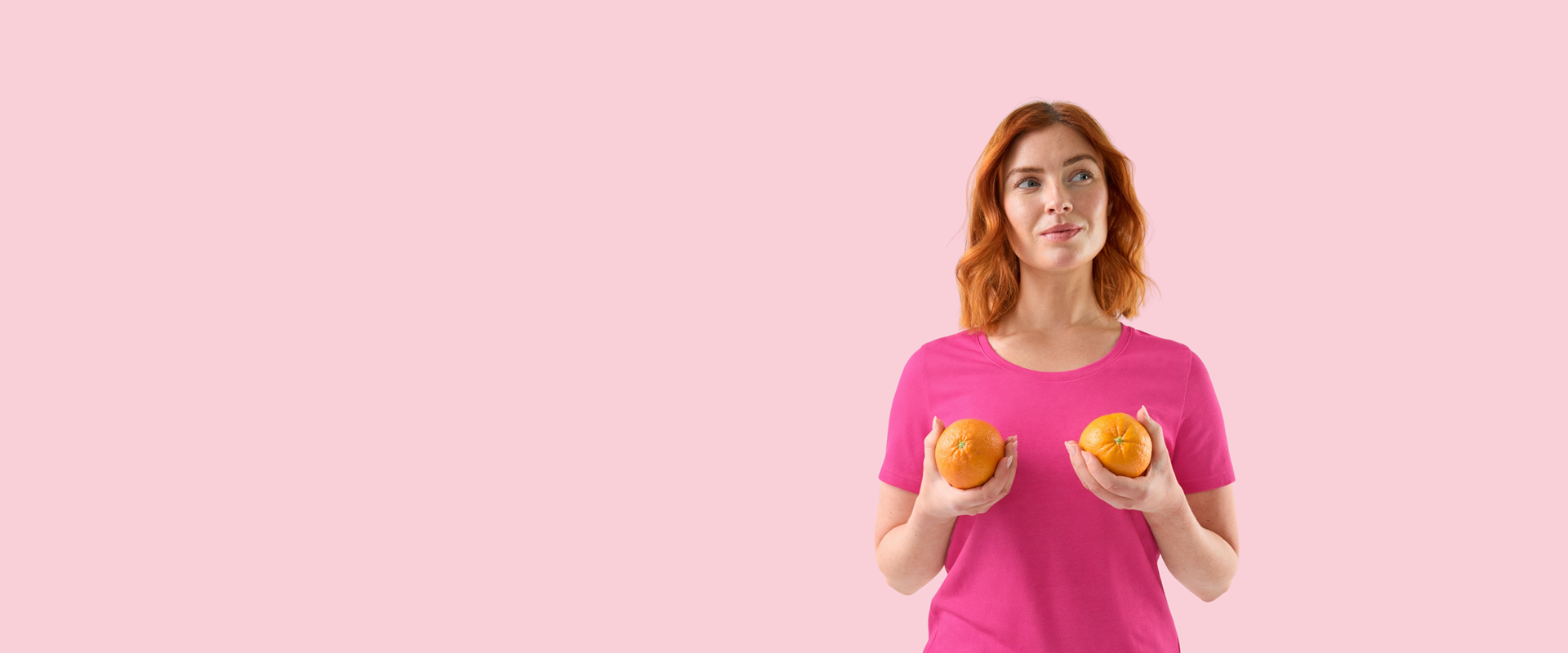kvinna i rosa t-shirt som håller två apelsiner mot bröstkorgen