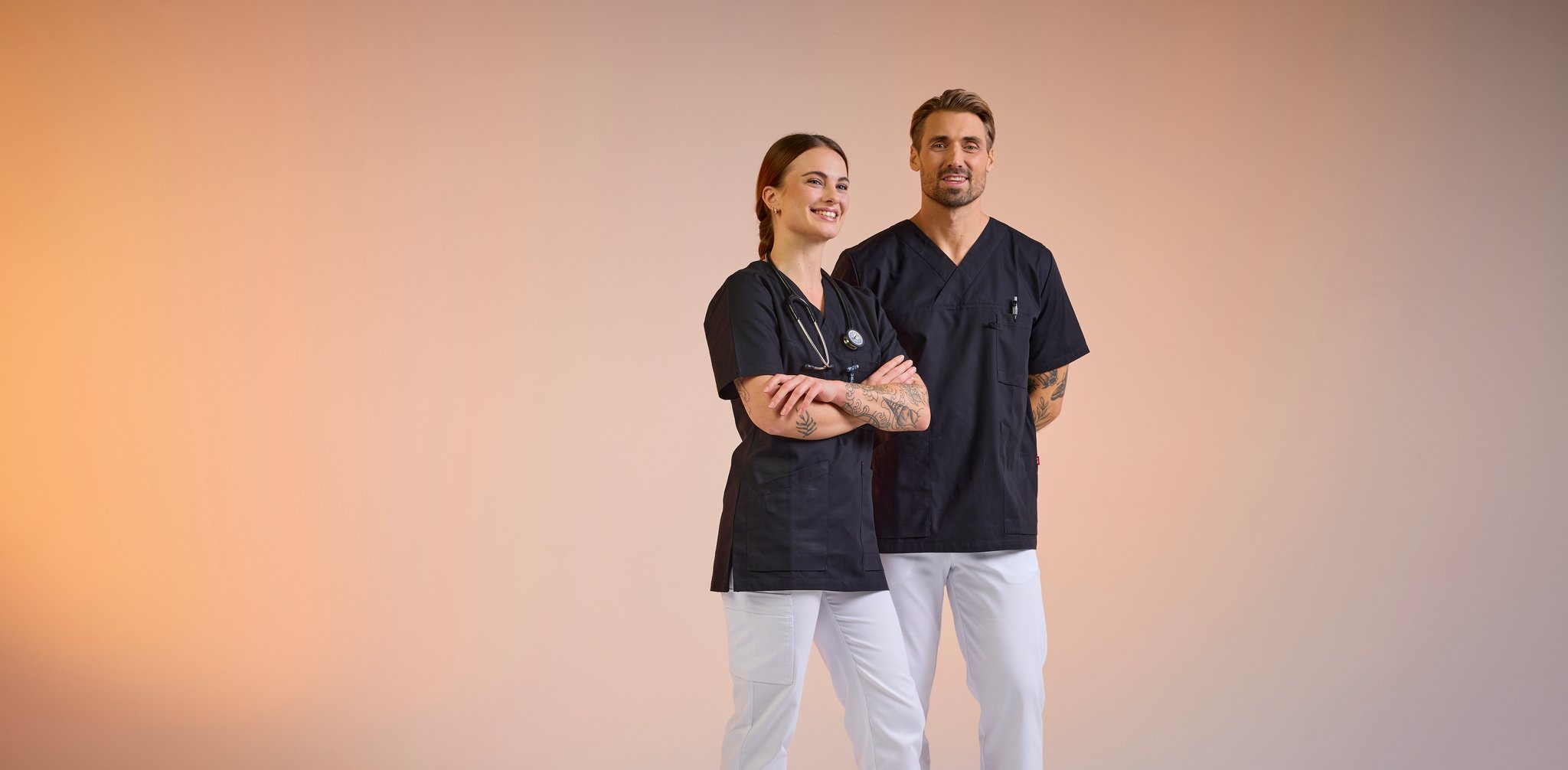 Woman and man in black tops and white care trousers from South West – stylish, comfortable and functional workwear for healthcare staff.