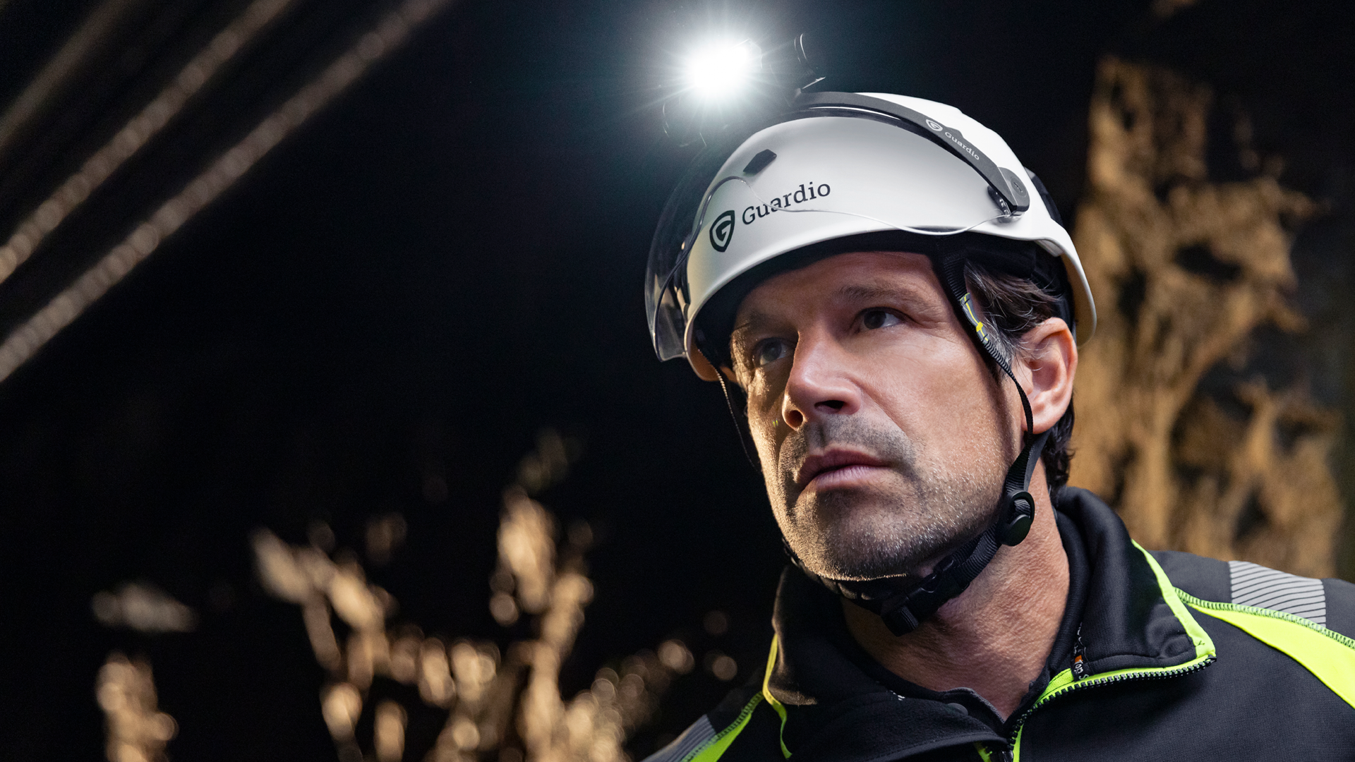 En man i arbetskläder och skyddshjälm med en pannlampa ser bestämd ut i en mörk tunnel