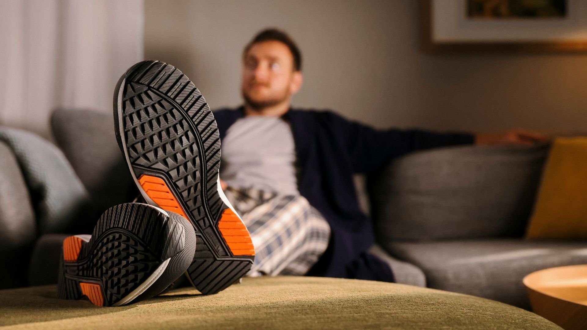 Kille som sitter i en soffa med ett par Monitor skor med svart/orange sula. Länk till Monitor-skor i produktlistning.