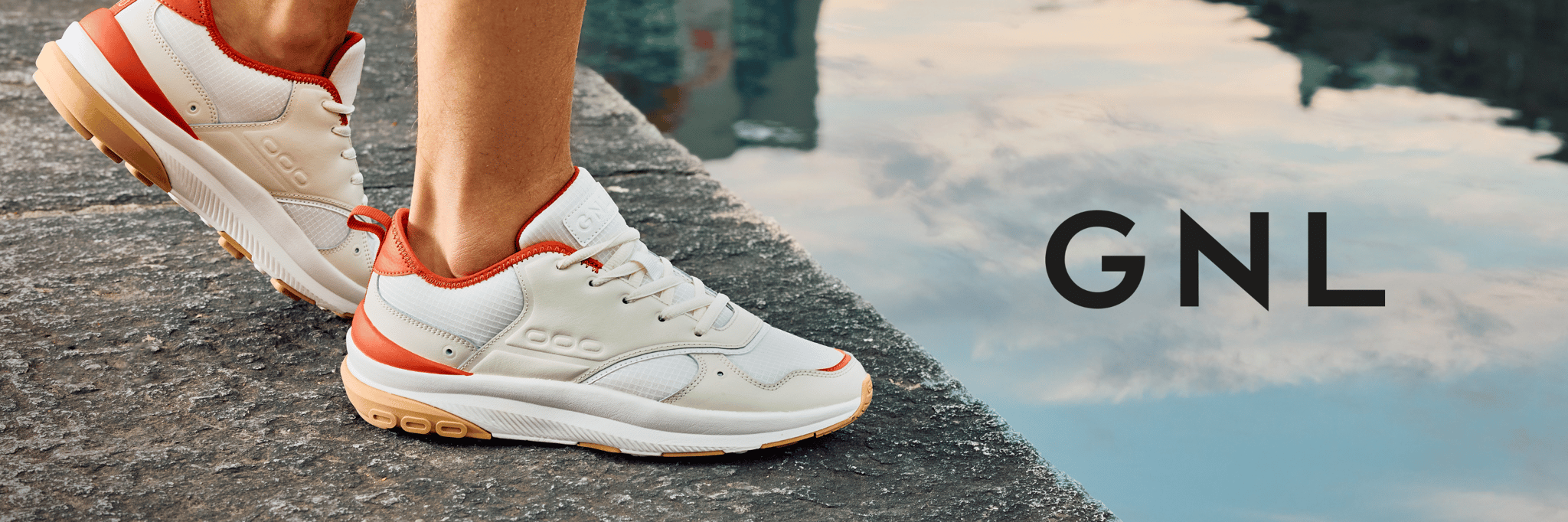 Valkoiset GNL-kengät, joissa punaiset yksityiskohdat veden äärellä, mukana GNL-logo.