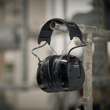 A pair of earmuffs from 3M hanging on iron pipes in an industrial environment