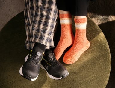 Vernesko i svart med gule detaljer og BOA®-system, ved siden av en person med oransje, fluffy sokker