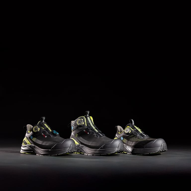 Tre skor ur Monitors ICE Evolution-serie står upplysta mot en mörk, svart bakgrund. Ljuset framhäver skornas design och detaljer, med varje modell placerad bredvid varandra för att visa skillnader i form och utförande.