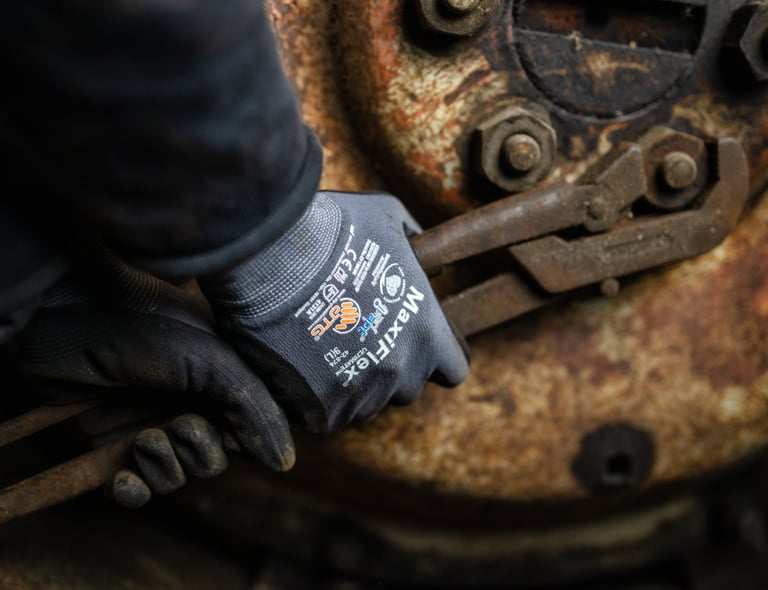 Nahaufnahme von Händen mit ATG MaxiFlex-Handschuhen, die mit rostigen Werkzeugen arbeiten – Langlebigkeit und Präzision in rauen Umgebungen. Anklickbares Bild mit Link zu ATG-Produkten im Webshop von Båstadgruppen.
