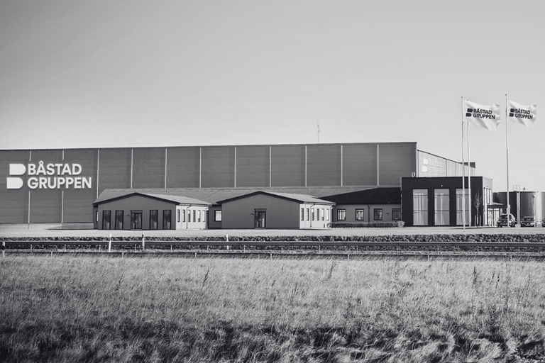 Der Hauptsitz und das Lager von Båstadgruppen in Ängelholm. Modernes Industriegebäude mit Firmenlogo und Fahnen, von außen fotografiert. Anklickbare Bildlinks zu weiteren Informationen über die Geschichte der Båstadgruppen.