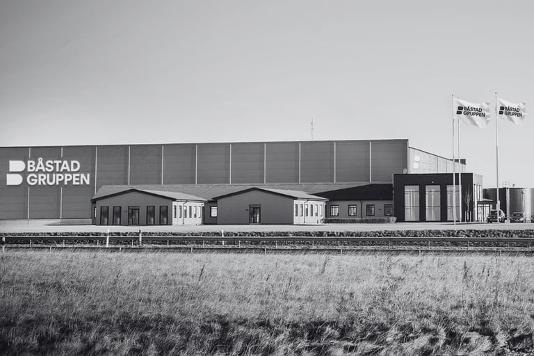 Der Hauptsitz und das Lager von Båstadgruppen in Ängelholm. Modernes Industriegebäude mit Firmenlogo und Fahnen, von außen fotografiert. Anklickbare Bildlinks zu weiteren Informationen über die Geschichte der Båstadgruppen.