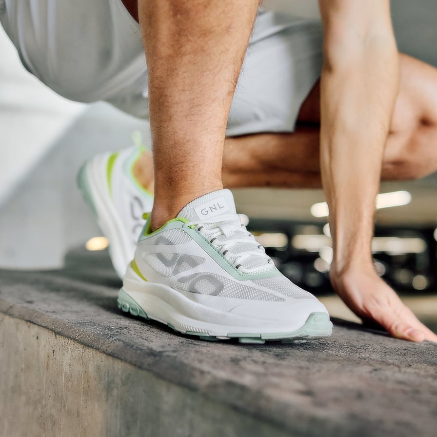 Henkilö kyykyssä, jalassa vaaleanvihreät kengät, joissa GNL-logo kielekkeessä.