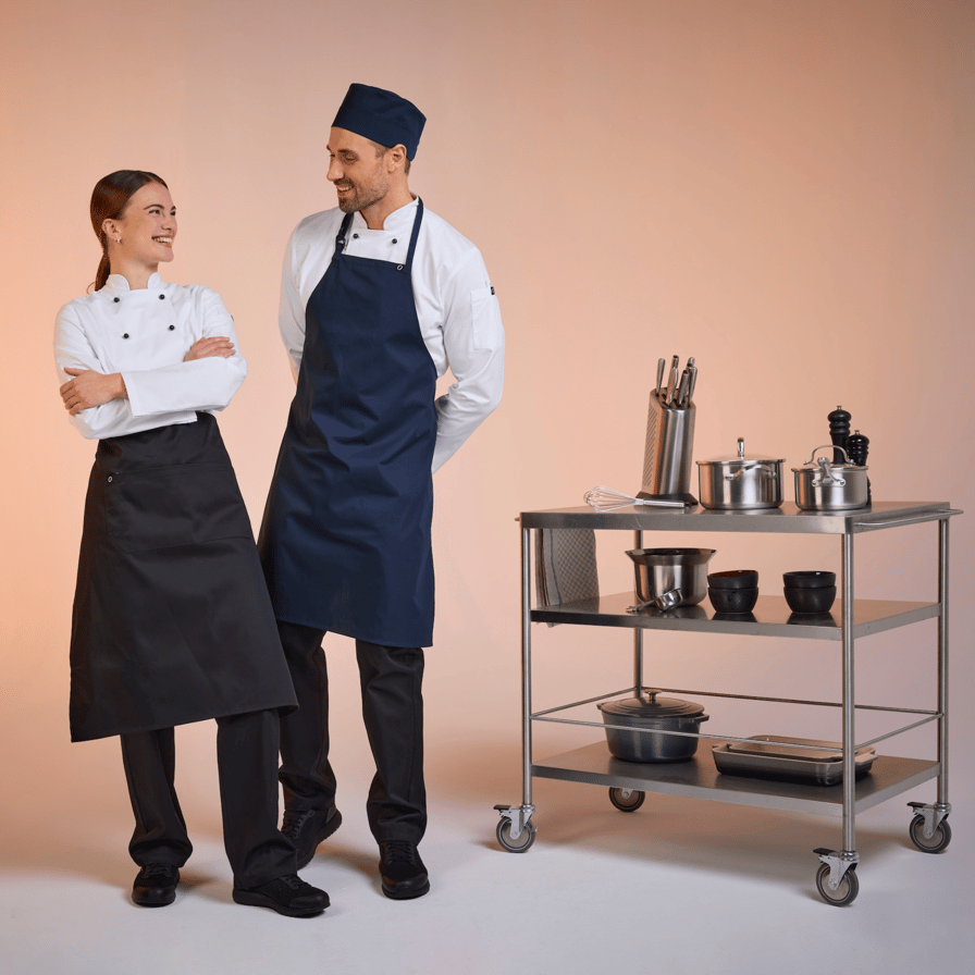 To restaurantmedarbejdere i mørke forklæder og hvide kokkejakker fra South West – funktionel unisexdesign til moderne køkkener.