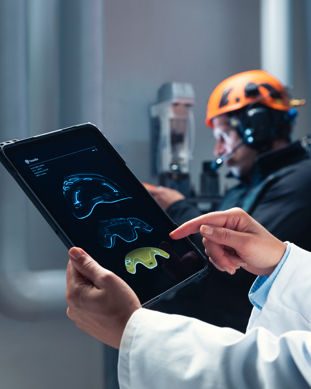 Nærbillede af tablet, der viser Mips-systemets lavfriktionslejer i en hjelm, med teknikere i baggrunden.