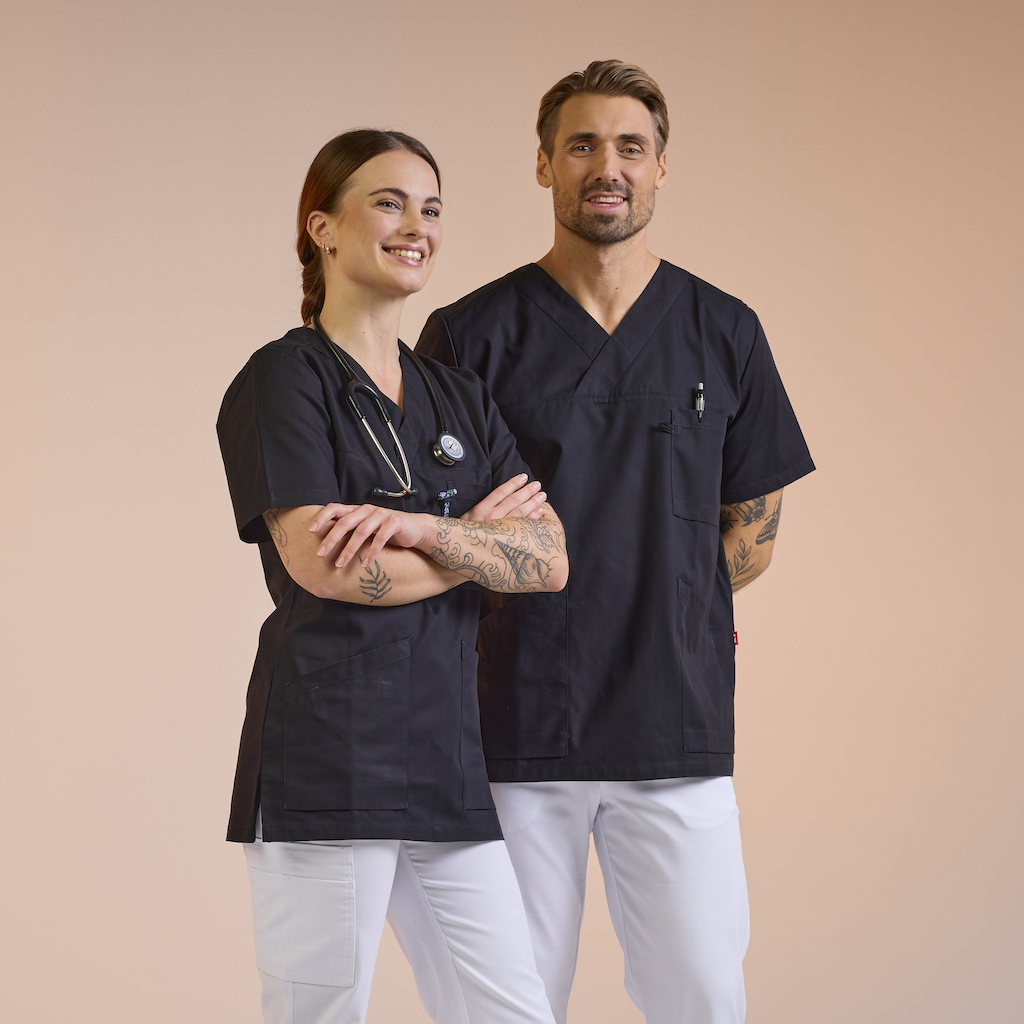 Mitarbeiter im Gesundheitswesen in Pflegekleidung aus dem South West – schwarze Tuniken mit weißen Hosen, entworfen für Komfort und Funktion. Klicken Sie auf den Link, um mehr über South West Pflege zu erfahren.