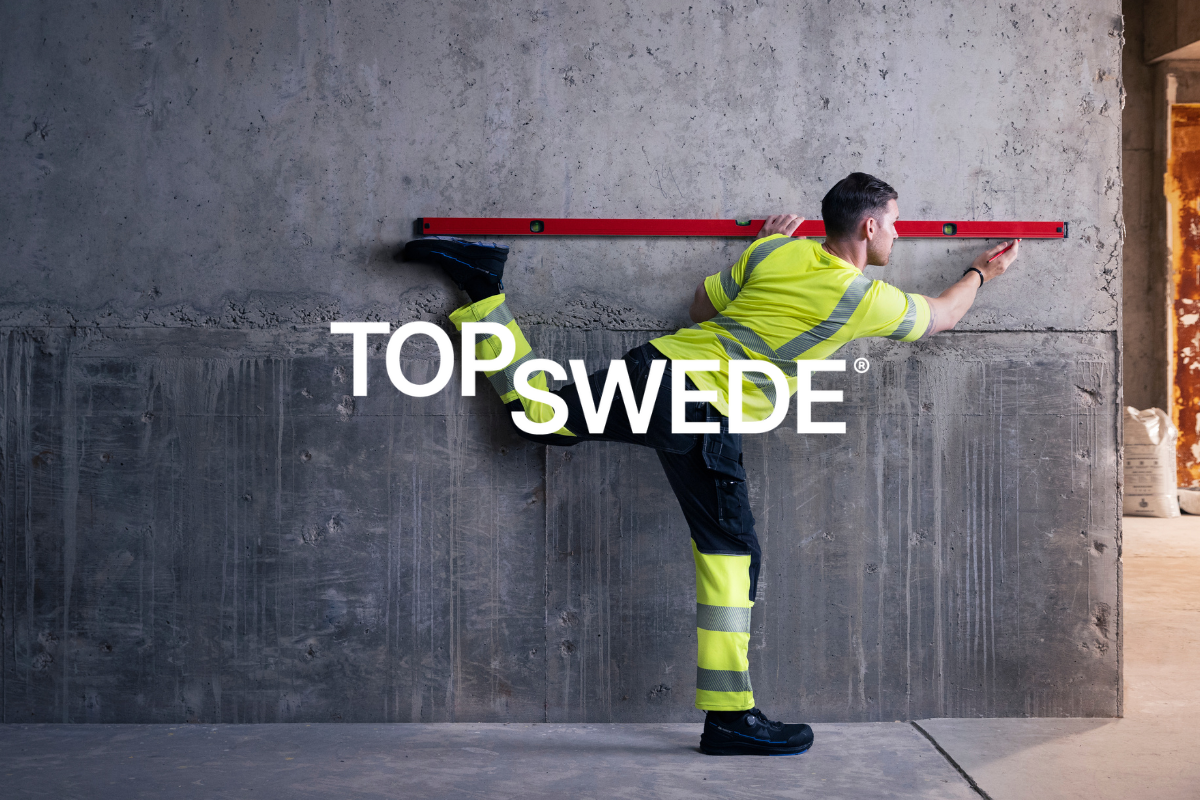 Construction worker in high-visibility gear and safety shoes balancing against a wall with a level. Clickable link to Top Swede products