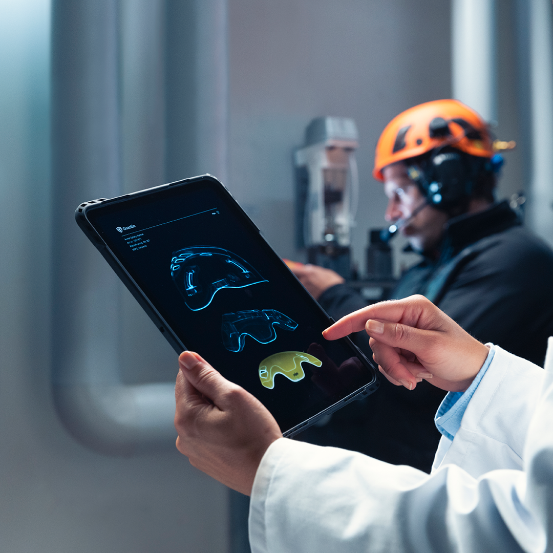 To personer i beskyttelsestøj, der gennemgår tekniske data på en tablet i et industrielt miljø