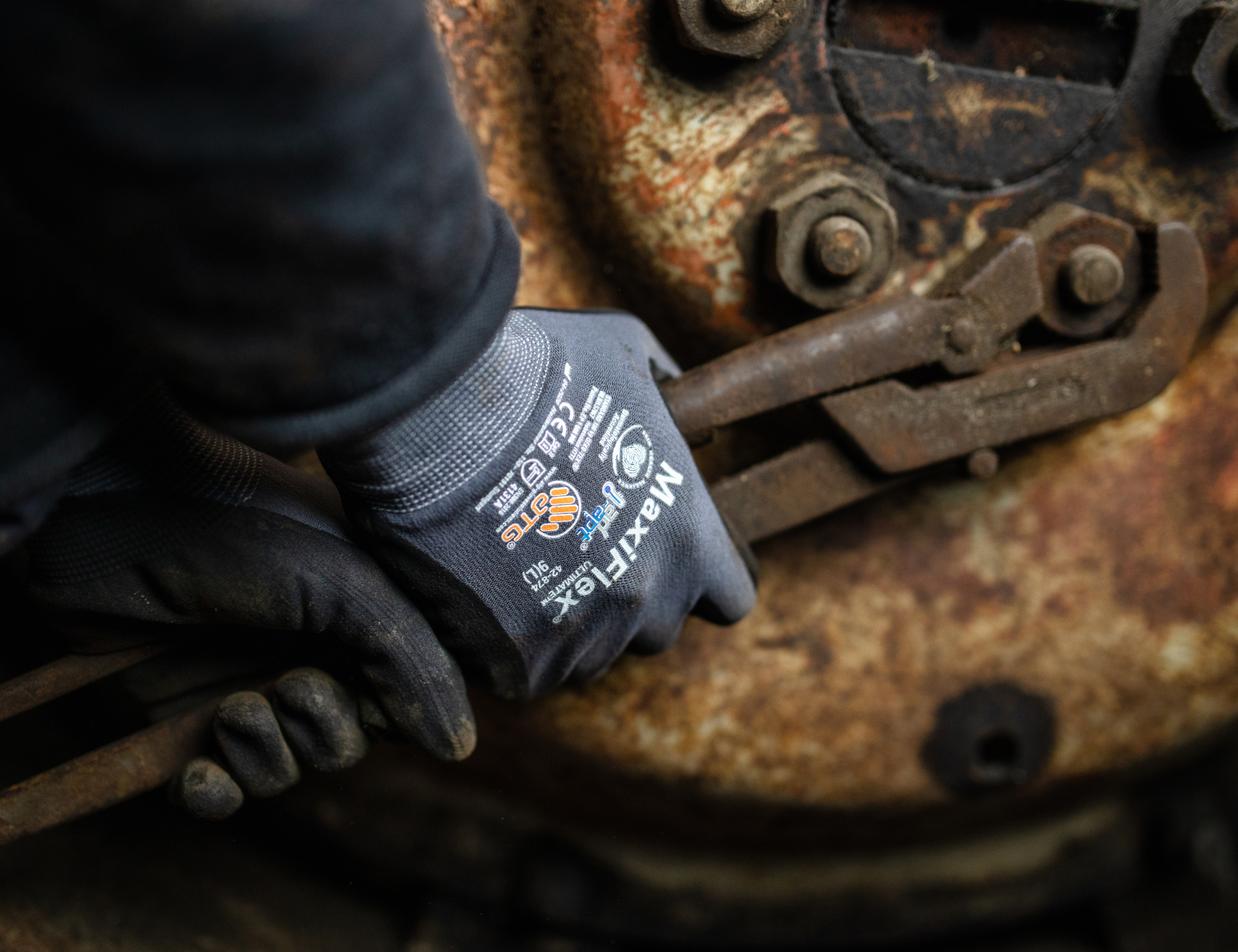 Lähikuva käsistä, joissa ATG MaxiFlex -käsineet, työskentelevät ruosteisilla työkaluilla – osoittavat kestävyyttä ja tarkkuutta vaativissa oloissa. Klikattava kuva vie Båstadgruppens verkkokauppaan.