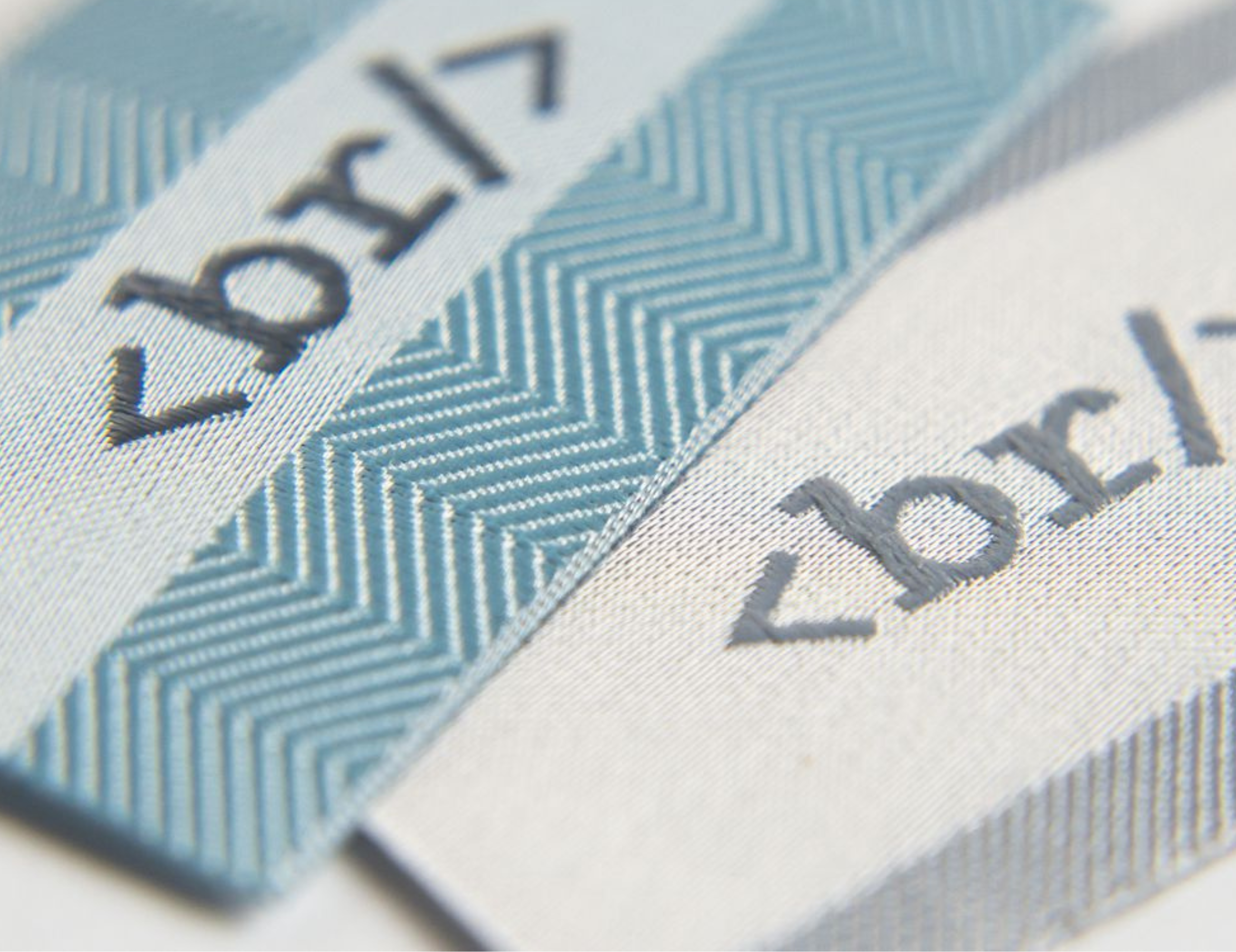Närbild på vävd etikett som är i färgerna vit och ljusblå