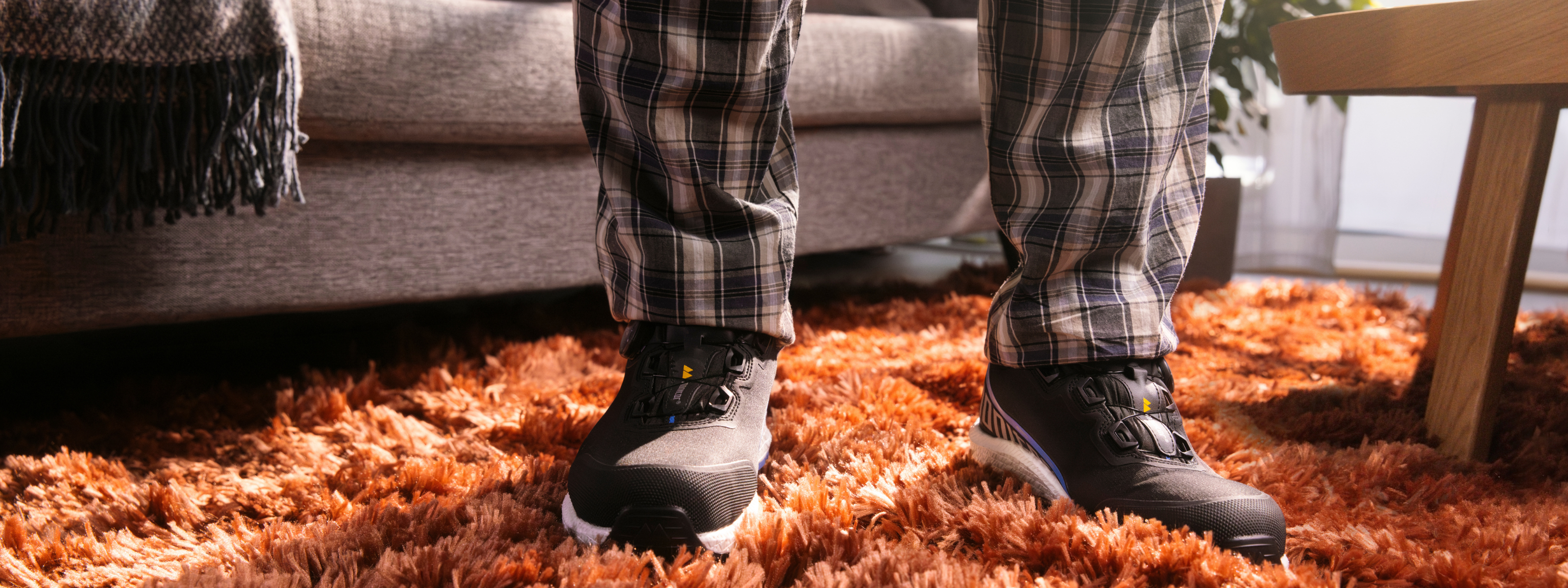 Man in checkered pajama pants stands on orange carpet wearing black safety shoes – clickable link