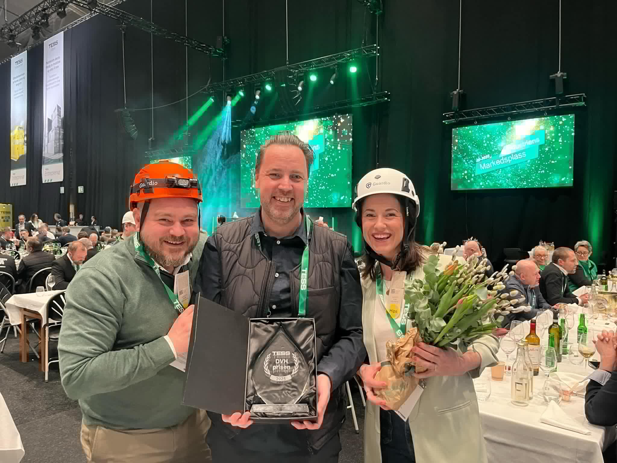 Kolme Båstadgruppenin työntekijää suojakypärissä pitelee DVH-palkintoa.