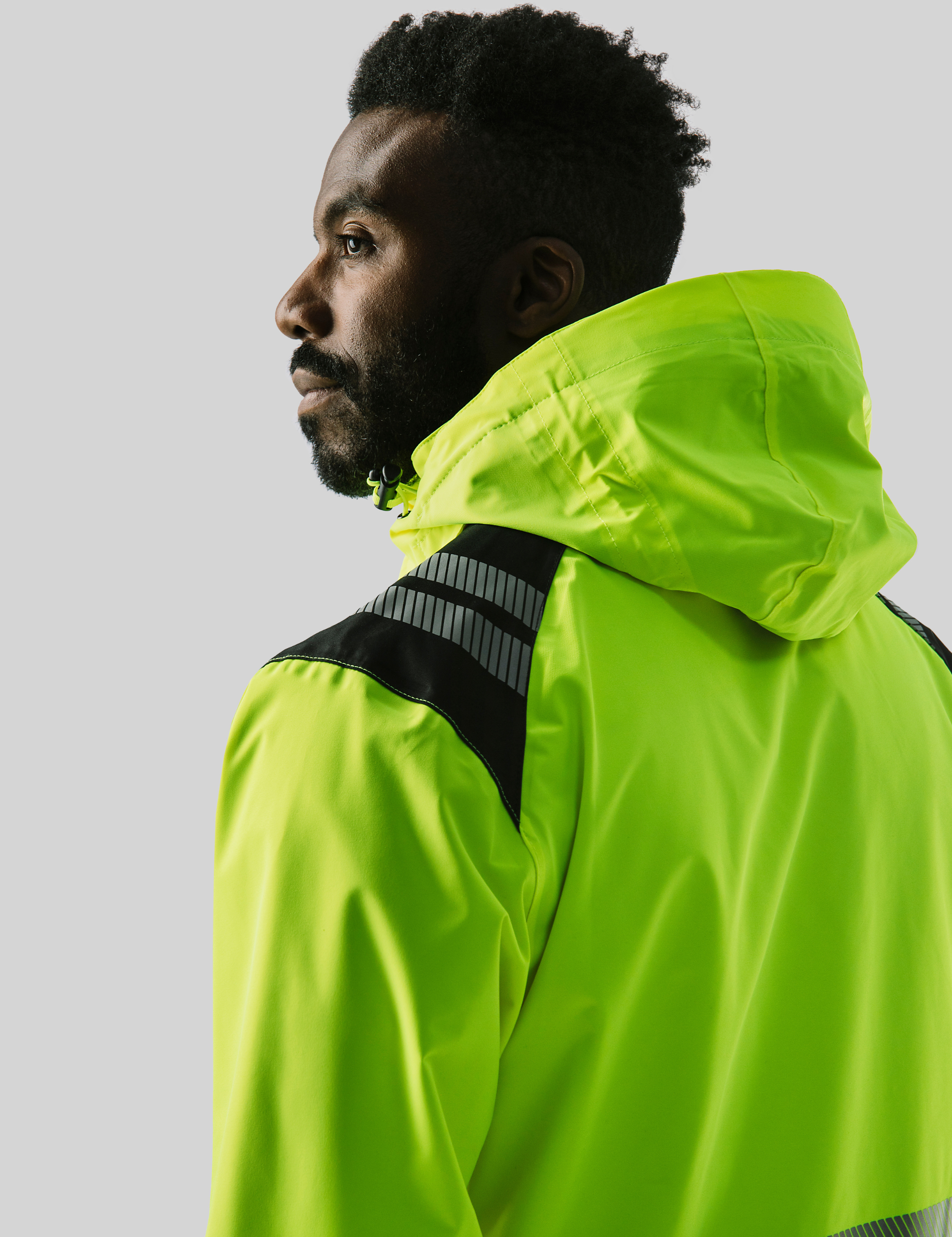 Nahaufnahme vom Rücken eines Mannes in einer gelben Warnschutzjacke mit Kapuze – zeigt die Passform und Sichtbarkeit der Jacke im Arbeitsumfeld.